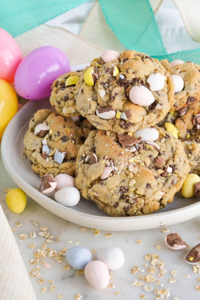 A plate of cookies with colorful candy eggs on top, surrounded by pastel-colored plastic eggs.