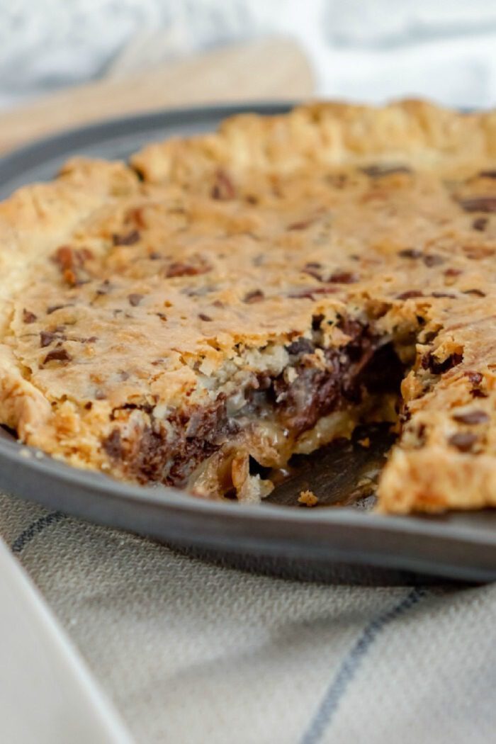 A baked chocolate and pecan pie with a slice missing, placed on a beige cloth.