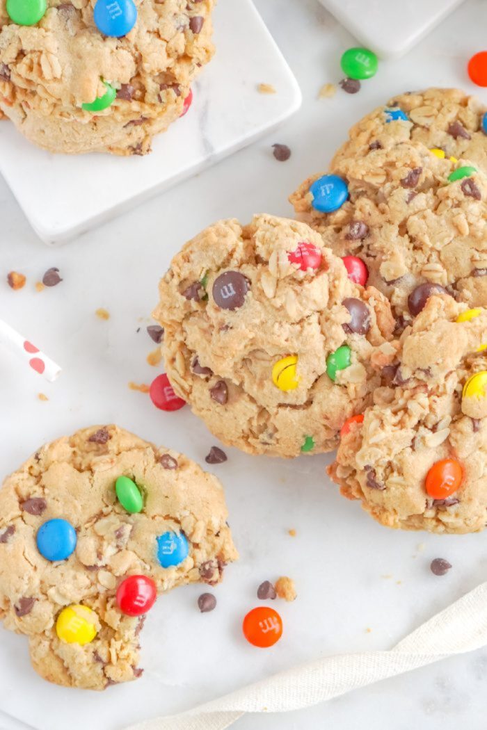 A close-up of cookies with colorful candy-coated chocolates and chocolate chips scattered around. One cookie has a bite taken out.