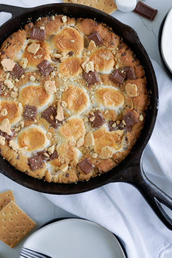 An overhead view of a s'mores skillet pie, topped with toasted marshmallows and chocolate pieces, placed on a white cloth.