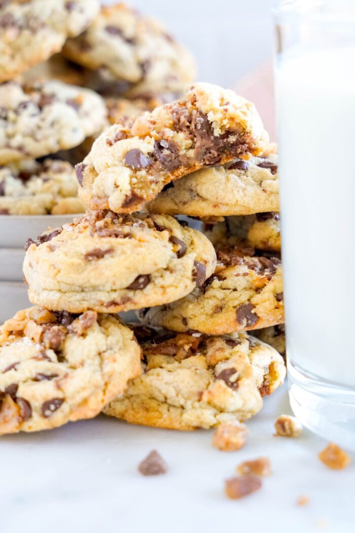 A close-up of chocolate chip cookies piled on top of each other, some partially eaten, next to a glass of milk.