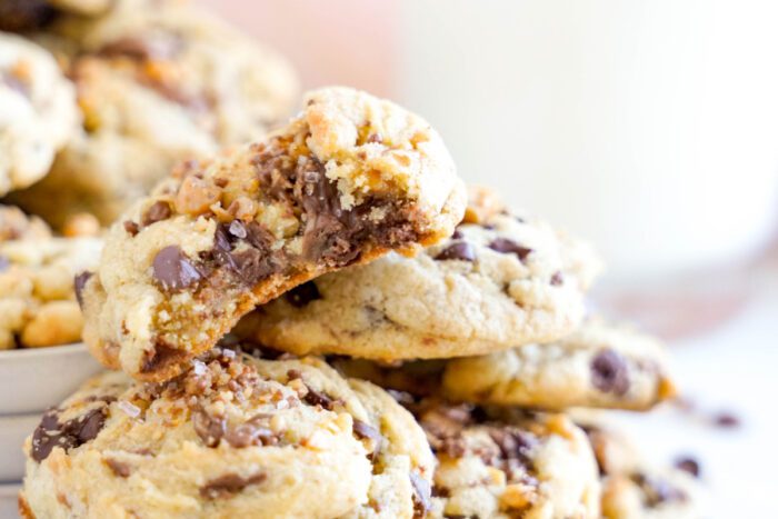 Close-up of chocolate chip cookies stacked on a plate. The top cookie has a bite taken out, revealing a soft, gooey center with melted chocolate chunks.