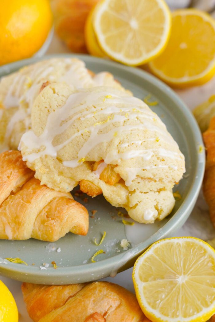 A plate with glazed lemon crookies surrounded by lemon halves and croissants.