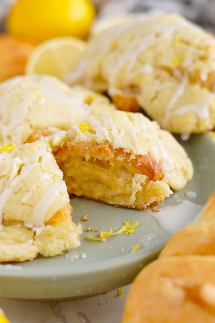 Close-up of lemon crookies drizzled with icing on a green plate. Yellow lemon peel zest is sprinkled on top and around the plate.