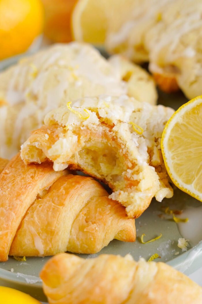 Close-up of pastries with a glaze and crumbles, surrounded by lemon slices. One pastry is partially eaten, revealing a soft, flaky interior.