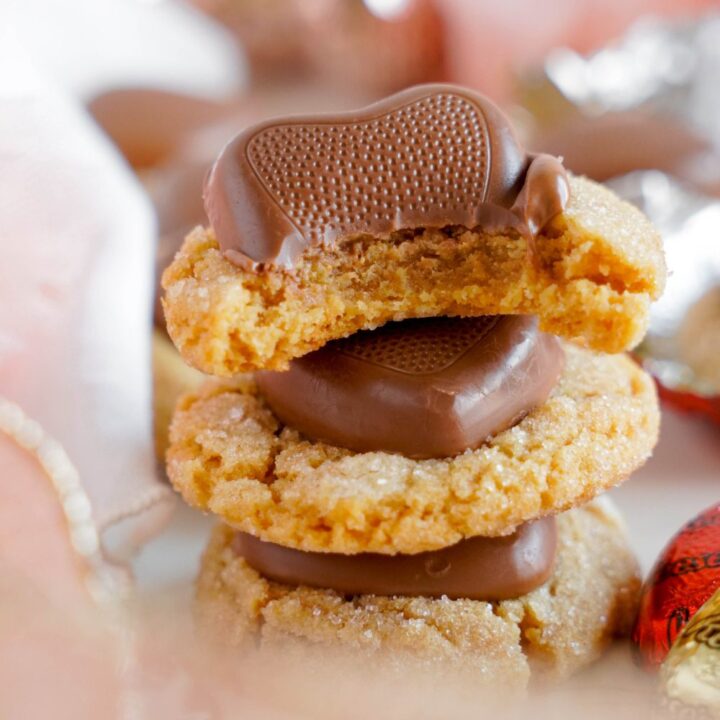 A heartwarming stack of peanut butter cookies topped with chocolates; one has a bite taken out, showcasing the irresistible charm of this Reese's-inspired recipe.